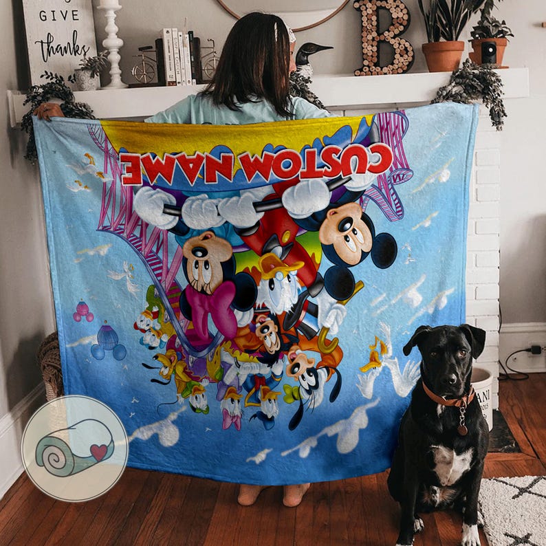 May include: A light blue blanket featuring Mickey Mouse, Minnie Mouse, Donald Duck, and Goofy. The blanket has a custom name printed in red and yellow. The design includes a bridge and clouds.