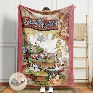 May include: A large, rectangular plush blanket featuring a vintage-style illustration with the text "Splash Mountain." The design includes various cartoon characters, a flying elephant, and a red border. The blanket is held up by a person.