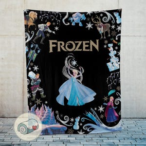 Op de afbeelding: Zwarte deken met personages en afbeeldingen uit de film "Frozen". Het ontwerp bevat Elsa in een blauwe jurk, sneeuwvlokken en het woord "FROZEN" in gouden letters. Andere personages omringen de centrale afbeelding.
