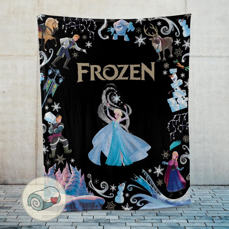 Op de afbeelding: Zwarte deken met personages en afbeeldingen uit de film "Frozen". Het ontwerp bevat Elsa in een blauwe jurk, sneeuwvlokken en het woord "FROZEN" in gouden letters. Andere personages omringen de centrale afbeelding.