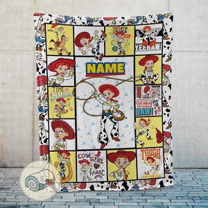 Op de afbeelding: Een witte deken met een collage van Jessie uit Toy Story. Het ontwerp bevat verschillende afbeeldingen van Jessie, de tekst "NAME" en een rand met een zwart-witte koeienprint. De deken is een gezellig, thematisch item.