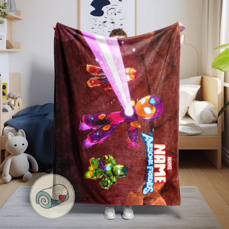 Op de afbeelding: Een Marvel-thema deken met een stripfiguur in een paars en oranje pak, die een roze straal uitzendt. De deken heeft de woorden "NAME" en "AWESOME FRIENDS" in wit en rood. De achtergrond is bruin.