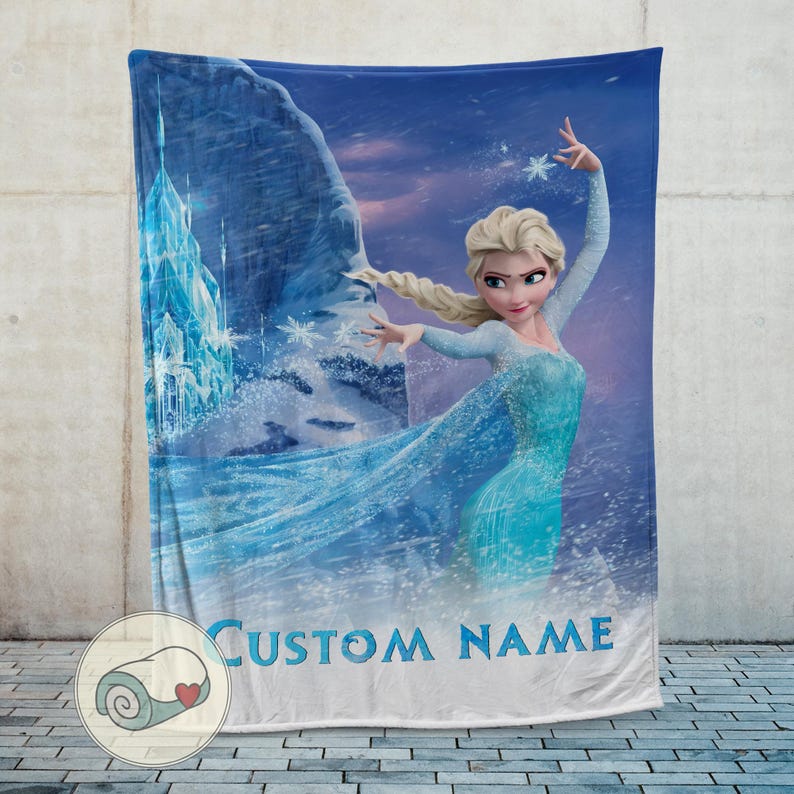 Puede incluir: Una manta polar azul con una imagen de dibujos animados de una mujer con un vestido azul, con un castillo y copos de nieve en el fondo. El texto "CUSTOM NAME" est&aacute; impreso en la parte inferior. La manta se muestra contra una pared neutra.