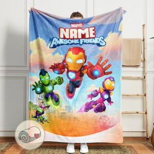 K&ouml;nnte beinhalten: Eine Marvel-Decke mit Iron Man und anderen Charakteren vor blauem Himmel. Die Decke zeigt die Worte "NAME" und "Awesome Friends". Die Decke wird von einer Person gehalten.