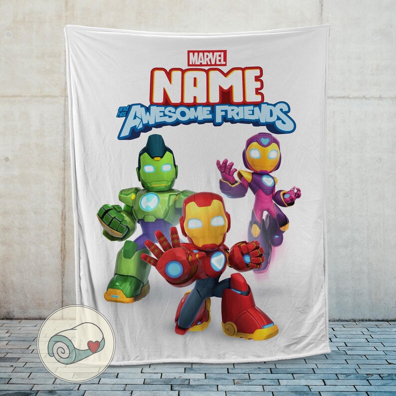 Op de afbeelding: Witte deken met drie striphelden: Iron Man, Hulk en een ander personage. De deken heeft het Marvel-logo en de woorden "NAME" en "Awesome Friends" in een kleurrijk lettertype. De deken wordt getoond tegen een lichtgrijze muur.