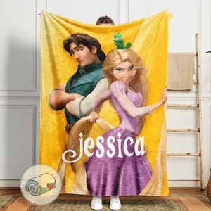 May include: A yellow fleece blanket featuring a cartoon image of a princess and a prince. The princess wears a purple dress, and the prince wears a blue vest. The blanket has the name "Jessica" in white script.