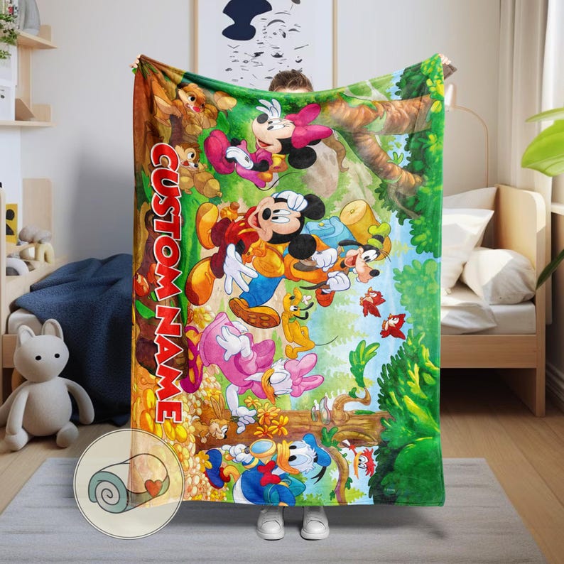 May include: A colorful blanket featuring Mickey Mouse, Minnie Mouse, Donald Duck, Goofy, and other Disney characters in a forest scene. The blanket has the text "CUSTOM NAME" in large, orange letters. The blanket is made of soft material.