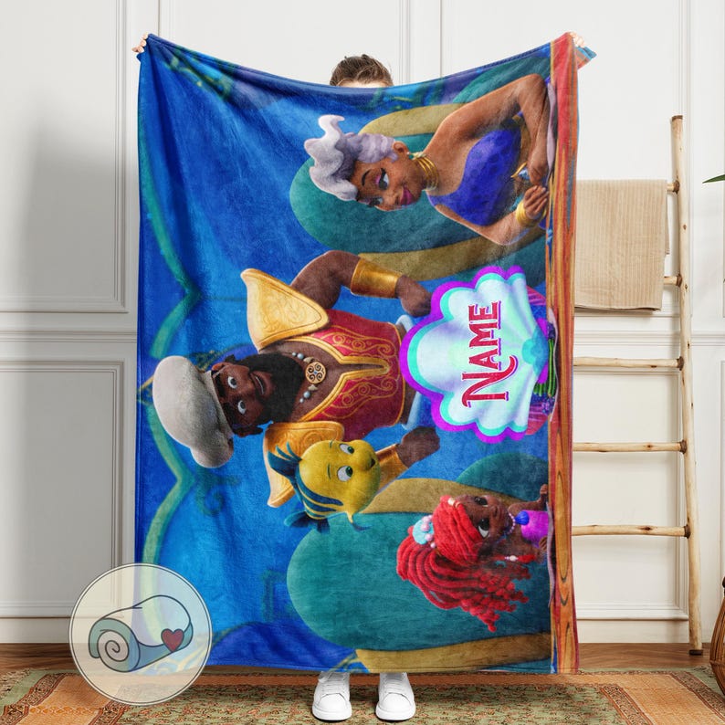 May include: A blue fleece blanket with cartoon characters from a popular animated film. The blanket has a repeating pattern and a personalised name graphic. The characters include a mermaid, a sea witch, and a prince.