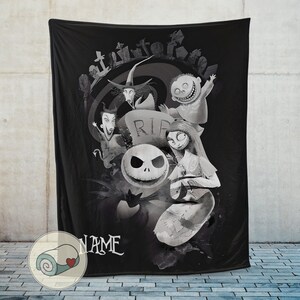 May include: Black throw blanket featuring a grayscale illustration of characters from The Nightmare Before Christmas. The design includes Jack Skellington, Sally, and other characters, with a graveyard scene in the background. The word "NAME" is written in white.