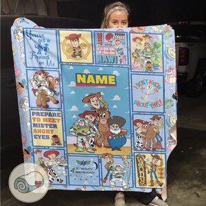 May include: A light blue blanket featuring characters from the Toy Story film series. The blanket displays images of Woody, Buzz Lightyear, and other characters, with phrases such as "You've got a Friend in Me" and "To Infinity and Beyond!"