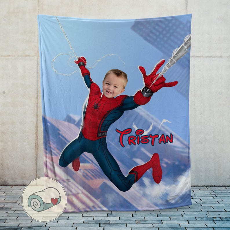 Op de afbeelding: Een gepersonaliseerde Spider-Man-deken met een kind in een Spider-Man-kostuum tegen een stadsachtergrond. De deken is voornamelijk blauw, rood en marineblauw, met de naam "Tristan" in rood script.