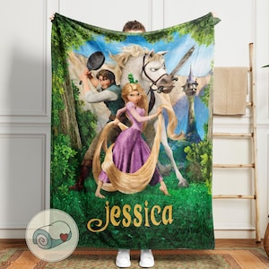 May include: A green fleece blanket featuring a colorful illustration of a princess, a man with a frying pan, and a white horse. The princess is wearing a purple dress and holding long, golden hair. The name "Jessica" is written in gold script.