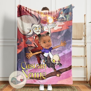 May include: A personalized fleece blanket featuring a cartoon illustration of a character with a child's face, a witch-like figure, and a skeletal creature. The blanket has a custom name in gold lettering and a rolled-up blanket graphic.