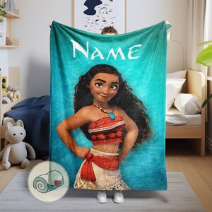 K&ouml;nnte beinhalten: Eine t&uuml;rkisfarbene Decke mit einer Cartoon-Illustration einer Frau mit langen, dunklen Locken, die ein rot-wei&szlig;es Outfit und eine Halskette mit einem blauen Anh&auml;nger tr&auml;gt. Das Wort "Name" steht in Wei&szlig; oben auf der Decke.