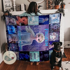 May include: A large, rectangular quilt featuring images of the Disney movie Frozen. The quilt has a central image of Elsa, surrounded by smaller images and text. The color scheme is predominantly blue and purple.
