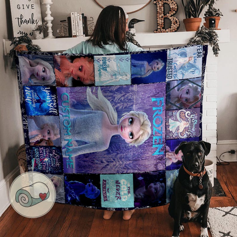 May include: A large, rectangular quilt featuring images of the Disney movie Frozen. The quilt has a central image of Elsa, surrounded by smaller images and text. The color scheme is predominantly blue and purple.