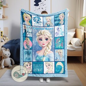 May include: A light blue blanket featuring Elsa from Frozen. The blanket has a central portrait of Elsa surrounded by smaller images and text, including "Custom Name" and phrases like "The cold never bothered me anyway."