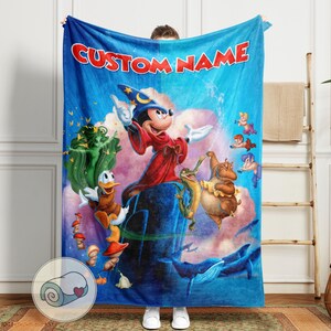 May include: A blue blanket featuring a colorful illustration of Mickey Mouse as a sorcerer, with other Disney characters. The blanket has the text "CUSTOM NAME" in red across the top. The blanket is held up by a person.