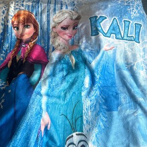 Pu&ograve; includere: Una coperta blu con i personaggi Anna ed Elsa del film Frozen. La coperta ha uno sfondo azzurro con fiocchi di neve e la parola "KALI" in blu. Anna indossa un vestito rosa e blu, ed Elsa un vestito blu.
