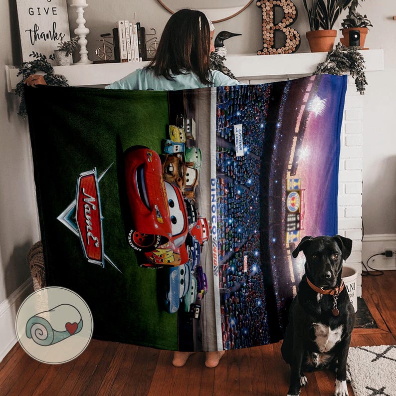 May include: A plush blanket featuring characters from the movie Cars. The blanket showcases Lightning McQueen and other characters on a green background, with a race track scene on the right side. The blanket is a vibrant mix of red, green, and blue.