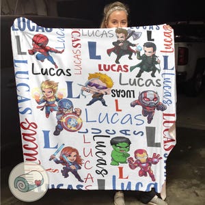 Puede incluir: Manta blanca con dibujos de superh&eacute;roes de dibujos animados y el nombre "Lucas" en varias fuentes y tama&ntilde;os. La manta incluye ilustraciones de Spider-Man, Capit&aacute;n Am&eacute;rica e Iron Man. El dise&ntilde;o incorpora la letra "L" y el nombre "Lucas" en un patr&oacute;n repetitivo.