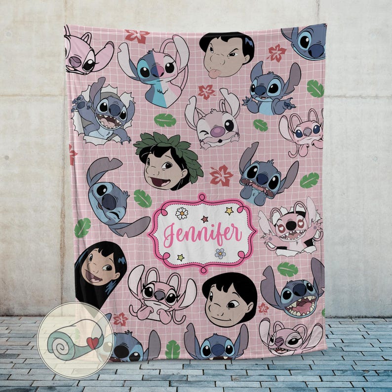 May include: Pink throw blanket featuring cartoon characters and floral designs. The blanket has a grid pattern and includes the name "Jennifer" in a decorative frame. The characters are in shades of blue, pink, and white.
