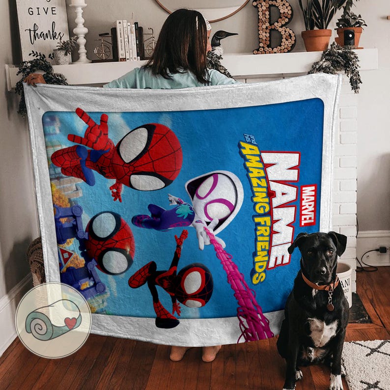 May include: A blue blanket featuring Marvel's Spider-Man and friends. The blanket has a white border and displays the words "NAME and AMAZING FRIENDS" in red and white. The blanket is held up by a person.
