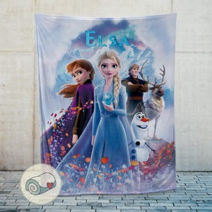 May include: A plush blanket featuring characters from the animated film "Frozen." The blanket showcases Elsa, Anna, Kristoff, Olaf, and Sven against a snowy mountain backdrop. The word "Elsa" is displayed in blue letters at the top.