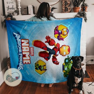 Peut inclure: Une couverture bleue avec un motif Iron Man de dessin anim&eacute;, le texte "Awesome Friends" et "Name", et le logo Marvel. La couverture a un fond bleu clair et un dessin de couverture roul&eacute;e dans le coin.