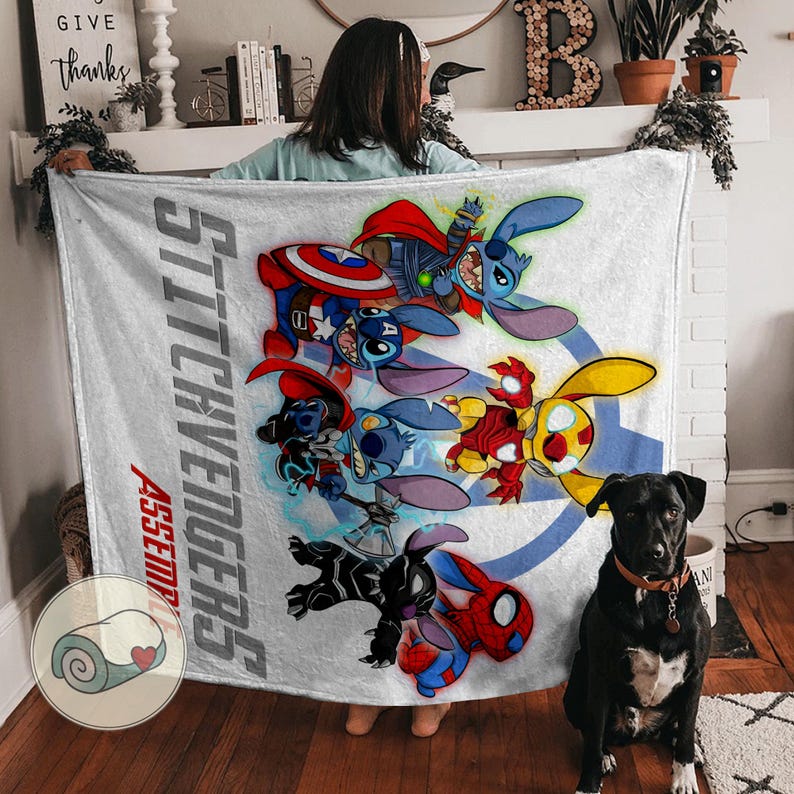 Puede incluir: Una manta blanca con un gr&aacute;fico colorido de personajes de Stitch vestidos como superh&eacute;roes de los Vengadores. La manta tiene el texto "Stitchvengers Assemble" en un dise&ntilde;o vertical. Un perro negro con un collar marr&oacute;n est&aacute; sentado frente a la manta.