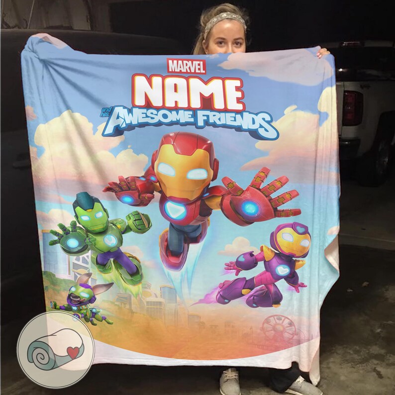 K&ouml;nnte beinhalten: Eine Marvel-Decke mit Cartoon-Illustrationen von Iron Man und anderen Charakteren. Die Decke hat einen blauen Himmelshintergrund und die Worte "Marvel" und "Name of Awesome Friends" sind darauf gedruckt.