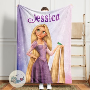 May include: A personalized blanket featuring a cartoon illustration of a princess with long blonde hair, wearing a purple dress, and holding a green chameleon. The name "Jessica" is written in purple script at the top. The background transitions from purple to pink.