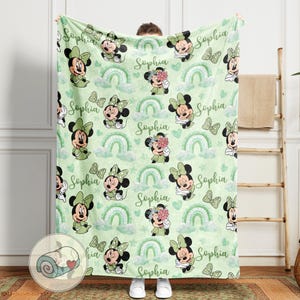 K&ouml;nnte beinhalten: Eine hellgr&uuml;ne Decke mit einem sich wiederholenden Muster aus Minnie Mouse, Regenbogen und Schmetterlingen. Der Name "Sophia" ist auf die Decke geschrieben. Die Decke besteht aus einem weichen Material, ideal f&uuml;r ein Kinderzimmer.