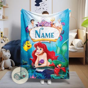 May include: A blue blanket featuring Ariel from The Little Mermaid, with characters including Flounder, Sebastian, and Prince Eric. The blanket has a personalised name banner and a rolled-up blanket graphic.