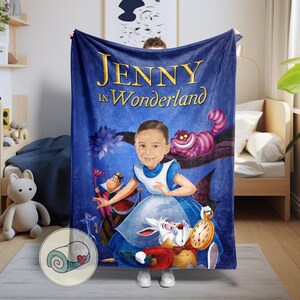 May include: A blue blanket featuring a custom illustration of a person as Alice in Wonderland, with the text "JENNY in Wonderland" in gold. The design includes the Cheshire Cat, the White Rabbit, and the Queen of Hearts.