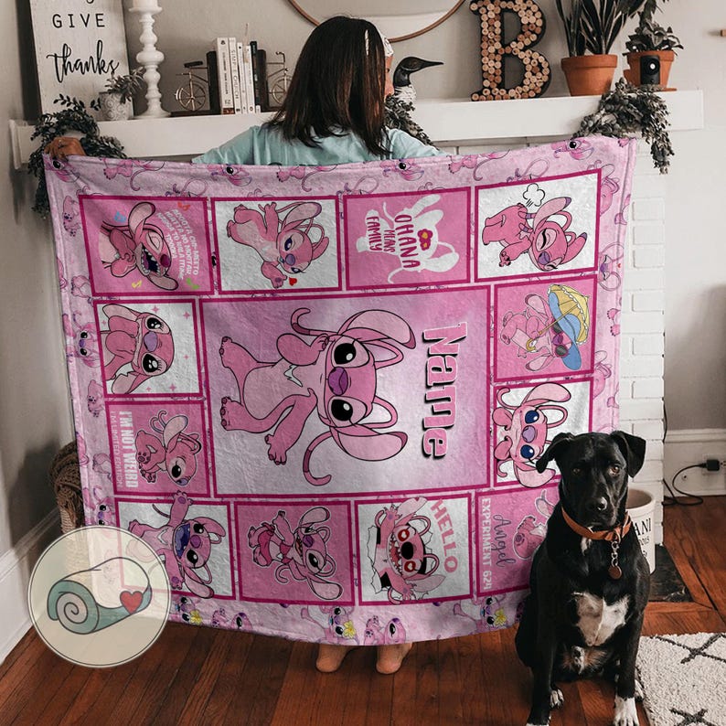May include: Pink fleece blanket featuring a cartoon character in various poses within square frames. The blanket has the word "Name" and the phrase "Ohana means family" printed on it. A black dog sits in front of the blanket.