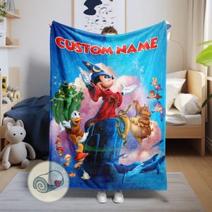 May include: A blue blanket featuring a colorful illustration of Mickey Mouse in a wizard's outfit, with other cartoon characters. The blanket has the text "CUSTOM NAME" in red. The blanket is held up by a person.