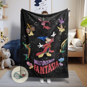 May include: Black blanket with characters and text from Walt Disney's Fantasia. The design includes Mickey Mouse in a sorcerer's outfit, along with other animated figures and the film's title in red and purple lettering. The blanket is held up by a person.