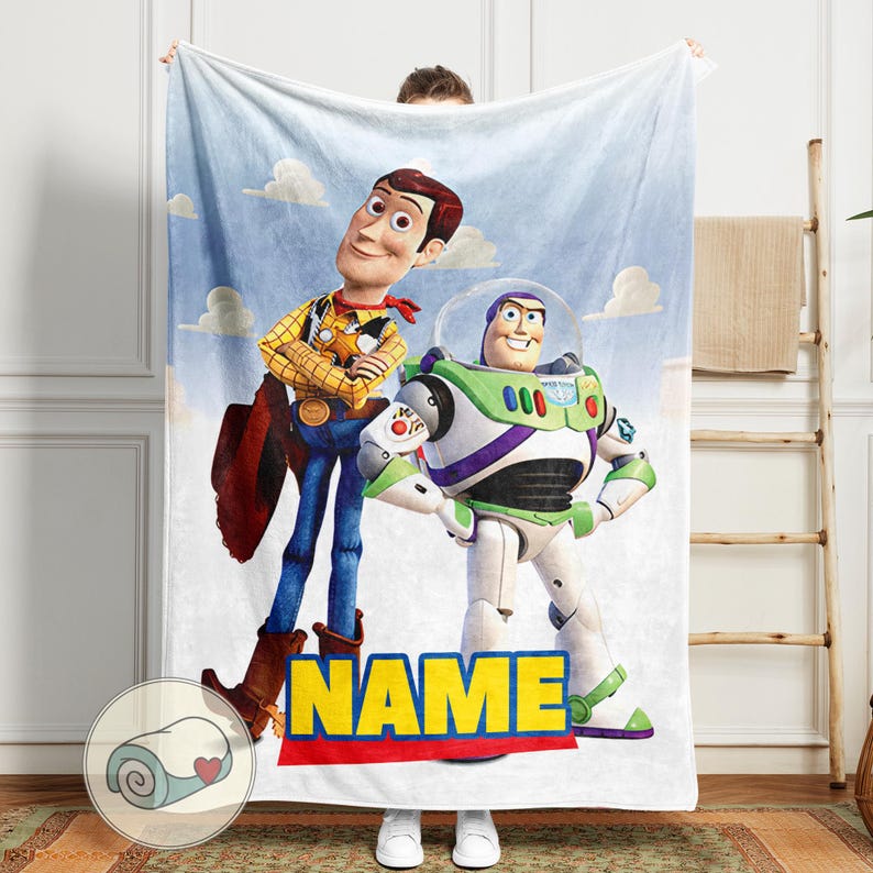 Pu&ograve; includere: Una coperta bianca con Woody e Buzz Lightyear di Toy Story su uno sfondo di cielo blu con nuvole. La coperta ha la scritta "NAME" in lettere gialle su sfondo rosso e blu.