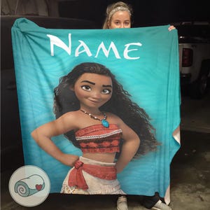 K&ouml;nnte beinhalten: Eine t&uuml;rkisfarbene Decke mit einem Cartoon-Bild einer Figur mit langen schwarzen Haaren, einem roten Oberteil und einem wei&szlig;en Rock. Das Wort "NAME" ist oben in Wei&szlig; aufgedruckt. Ein kleines Logo einer gerollten Decke befindet sich in der unteren linken Ecke.