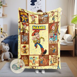 May include: A yellow and brown blanket featuring a cartoon cowboy character. The blanket has a repeating pattern of the character in various poses, with the word "NAME" in a central box. The blanket is made of a soft material.