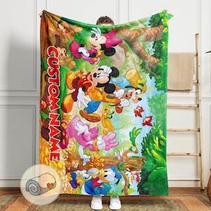 May include: A colorful blanket featuring Mickey Mouse, Minnie Mouse, Donald Duck, Daisy Duck, Goofy, and Pluto in a forest scene. The blanket has the text "CUSTOM NAME" in a vertical font. The blanket is a cozy, soft throw.