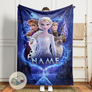 Pu&ograve; includere: Una coperta in pile blu con personaggi di un popolare film d'animazione. La coperta mostra Elsa, Anna, Kristoff, Olaf e Sven, con la parola "NAME" al centro. Il design include una scena di montagna innevata e un logo a forma di cuore.