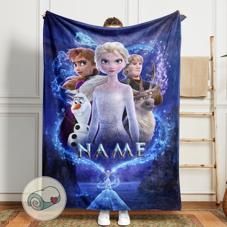 Pu&ograve; includere: Una coperta in pile blu con personaggi di un popolare film d'animazione. La coperta mostra Elsa, Anna, Kristoff, Olaf e Sven, con la parola "NAME" al centro. Il design include una scena di montagna innevata e un logo a forma di cuore.