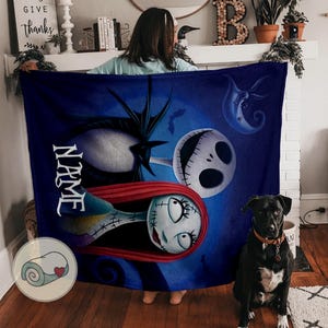 May include: A dark blue blanket featuring characters from The Nightmare Before Christmas. The blanket has images of Jack Skellington, Sally, and other themed elements. The word "NAME" is printed vertically on the blanket.