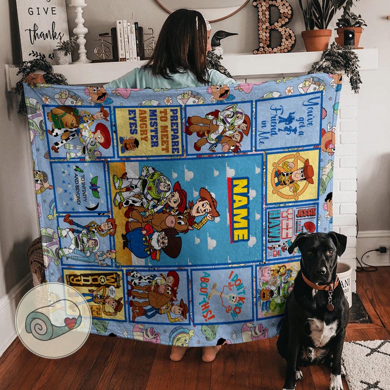 May include: A light blue blanket with Toy Story characters. The blanket has a central panel with the word "NAME" and various character illustrations. Other panels include phrases like "You've got a Friend in Me" and "To Infinity and Beyond."