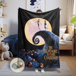 K&ouml;nnte beinhalten: Schwarze Fleece-Decke mit einer Szene aus "The Nightmare Before Christmas". Das Design zeigt Jack und Sally vor einem Vollmond, mit dem Filmtitel in goldfarbenen Buchstaben. Die Decke wird von einer Person gehalten.