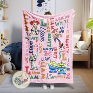 May include: A pink blanket featuring characters from the animated film "Toy Story." The blanket has the name "Liam" printed in various fonts and colors. The blanket features images of Woody, Buzz Lightyear, Jessie, and the aliens.