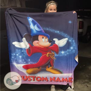 Pu&ograve; includere: Una grande coperta blu navy con una vivace illustrazione di Topolino vestito da mago. Mickey indossa un cappello blu con una luna crescente e stelle, una veste rossa e scarpe gialle. Il testo "CUSTOM NAME" &egrave; visibile in basso.