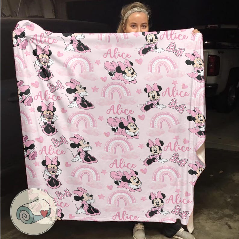 K&ouml;nnte beinhalten: Eine rosa Decke mit einem sich wiederholenden Muster von Minnie Mouse, Schleifen, Regenbogen, Sternen und dem Namen "Alice". Die Decke hat ein weiches, pl&uuml;schiges Aussehen mit einer wei&szlig;en Unterseite. Das Design ist in Rosa- und Schwarzt&ouml;nen gehalten.